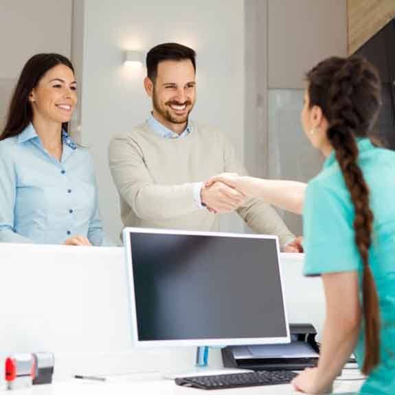 a couple of patients greeting a front desk team member