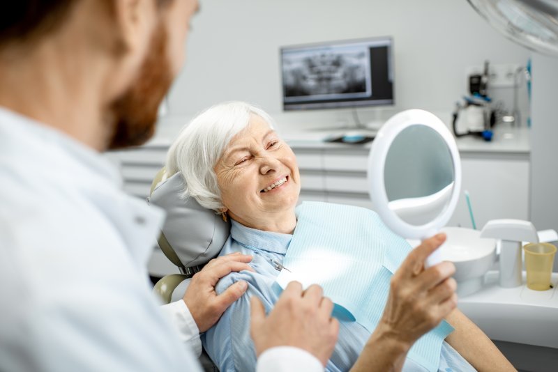 An older woman admiring her new dental implant in a hand mirror