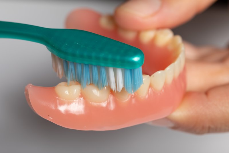 patient cleaning dentures with a toothbrush